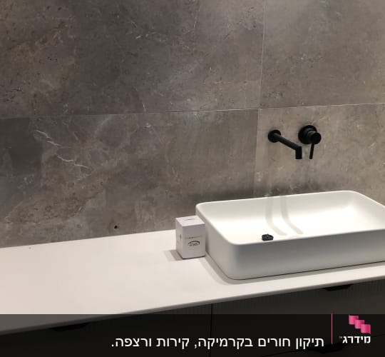 קיר שיש אפור עם כיור לבן וברז שחור